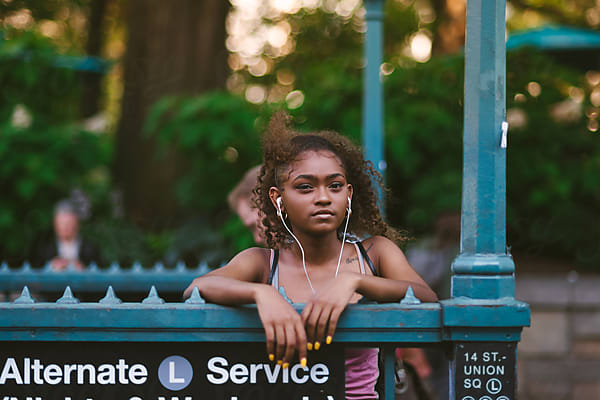 A teenage girl leans on a railing with earbuds in