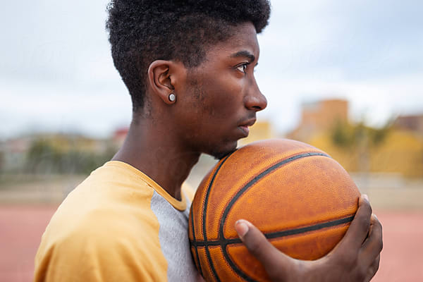 A teenage boy holds a basketball, looking off into the distance