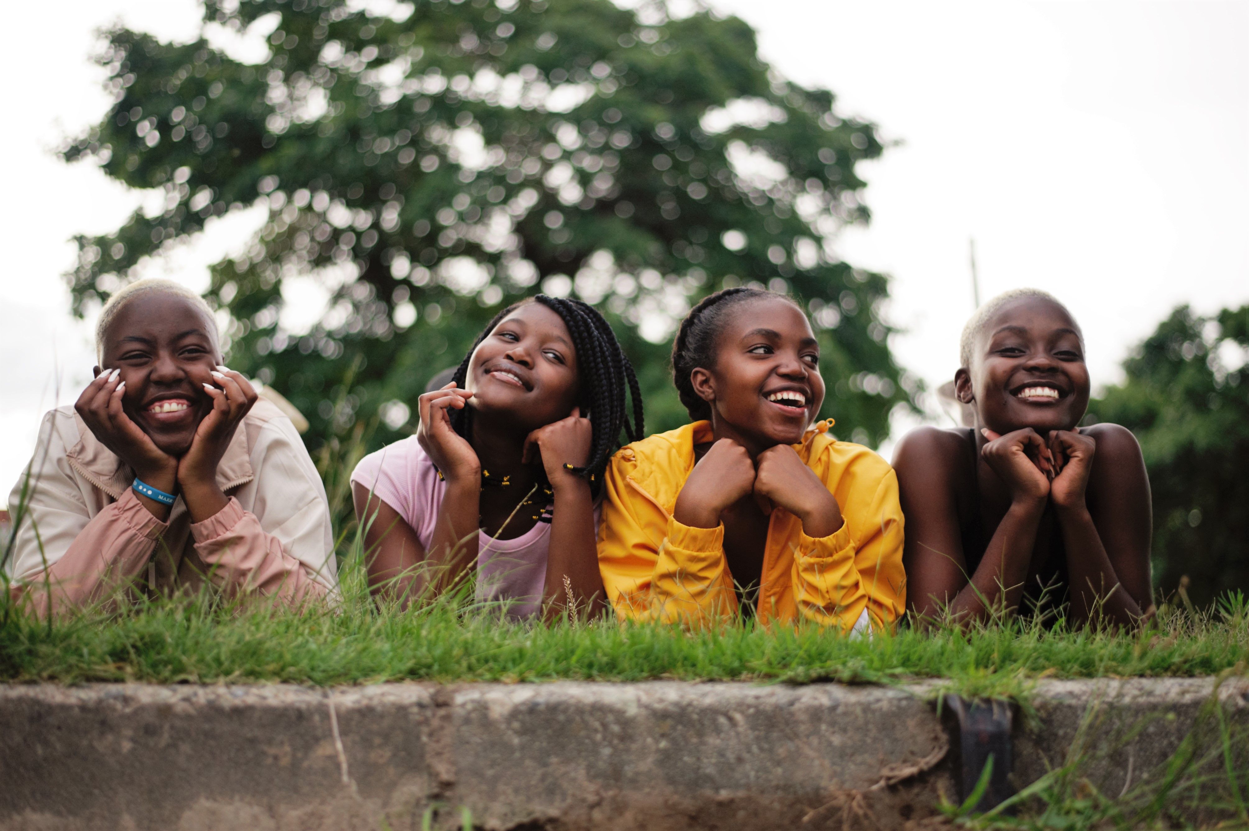 Four smiling Black teenage girls lying in the grass together