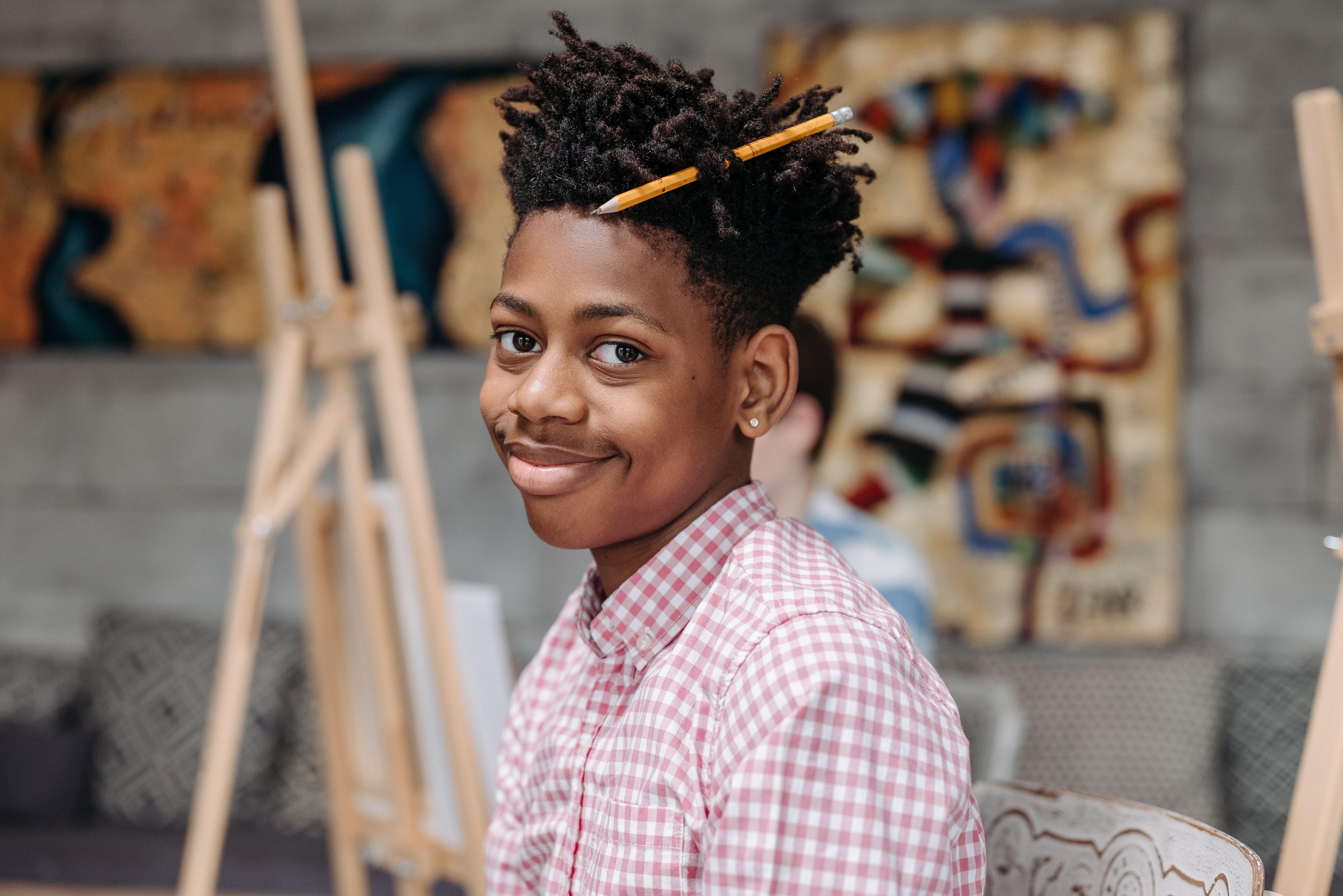 A teenage boy smiles over his shoulder in an art class, a pencil tucked in his hair